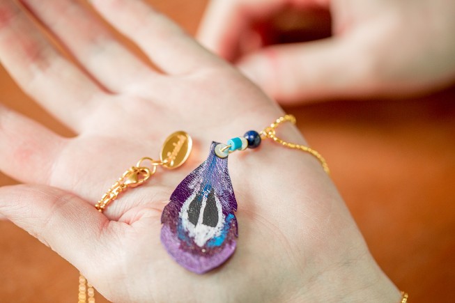 Un collier Faraboule fait d'une plume de cuir découpée et peinte à la main.