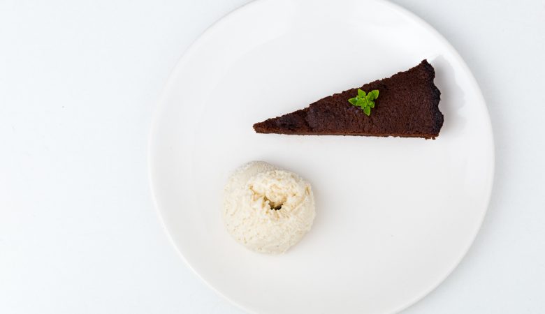 Photographie épuré d'une part de gâteau à la courgette et au chocolat accompagné d'une boule de glace.